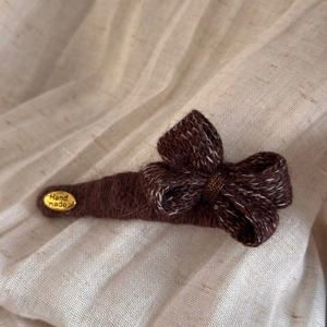 Détail d'une pince à cheveux nœud tricoté marron foncé avec étiquette dorée