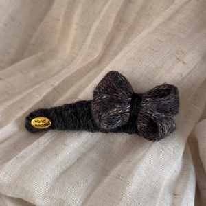 Détail de la pince à cheveux noeud en tricot gris avec étiquette dorée Hand Made
