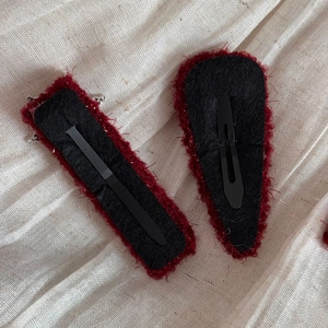 Detail view of red knitted winter hair clips showing the black felt back and metal clip base