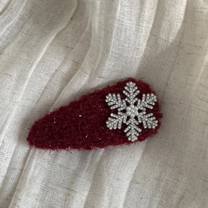 Close-up of a plush red hair clip with a sparkling silver snowflake and pearl detail
