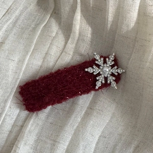 Macro detail of wine red plush hair clip featuring a silver snowflake with shiny rhinestones