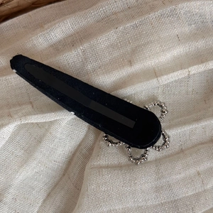 Detailed view of a black teardrop hair clip with silver floral metal accents on linen