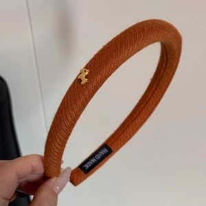 Dettaglio fascia in maglia arancione bruciato con ciondolo a cane dorato ed etichetta handmade