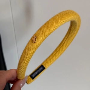 Vista macro del cerchietto in maglia a coste giallo con uccellino dorato ed etichetta