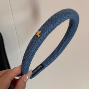 Dettaglio del cerchietto in maglia blu con etichetta fatta a mano e fibbia a cane dorata