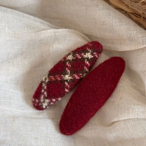 Detailed view of red plaid wool hair clip and dark red felt hairpin on linen fabric
