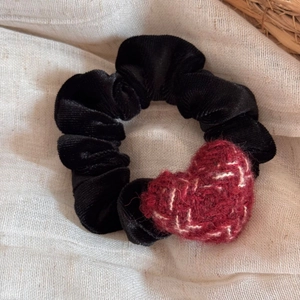Detail of black velvet scrunchie with a red knitted heart charm on a linen background