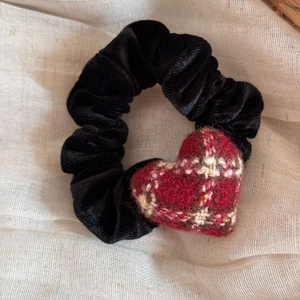 Detailed texture of black corduroy scrunchie with red plaid heart ornament on beige fabric