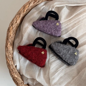 Dettaglio di tre mollette per capelli in lana a forma di mini borsa, viola e bordeaux