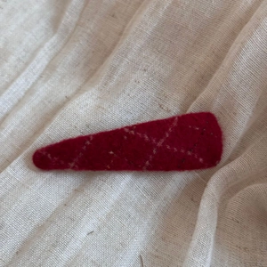 Macro detail of a burgundy wool felt hair clip with vintage stitching on soft fabric