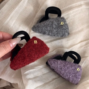 Dettaglio della texture in lana e del logo dorato su mini fermagli per capelli in peluche
