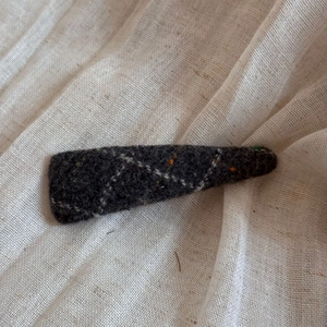 Close-up of wool hair clip featuring diamond stitching and colorful dots on grey fabric