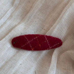 Detail of red wool felt hair clip with elegant hand-embroidered plaid on beige fabric