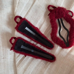 Detailed back view of three dark red plush hair clips with ribbon bows and metal fasteners