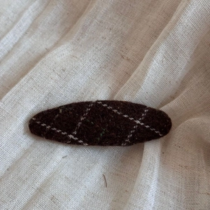 Macro detail of dark brown tweed hair clip with white stitching on soft linen fabric