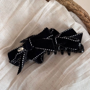 Macro detail of black velvet bow hair claw clip with white dotted stitching and silver tag