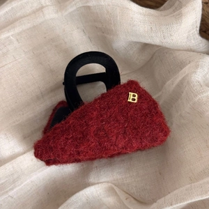 Dettaglio ravvicinato della molletta in peluche bordeaux con lettera B in metallo dorato