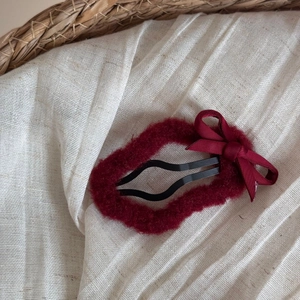 Close-up of a burgundy plush hair clip with a silk bow on cream linen fabric background