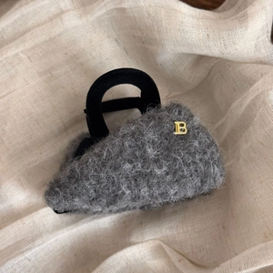 Dettaglio della molletta per capelli in peluche grigio con lettera B in metallo oro