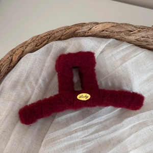 Close-up of a burgundy plush hair claw clip featuring a lucky golden metal nameplate