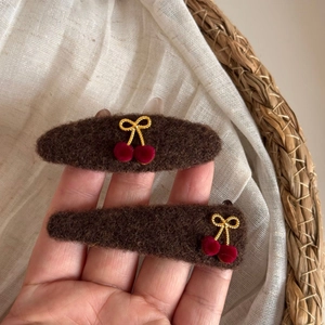 Detailed macro view of plush cherry and bow hair clips in coffee brown knit material