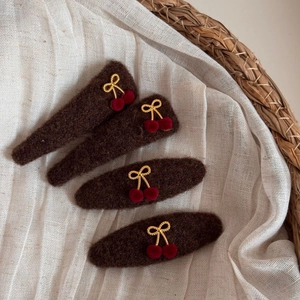 Winter cherry bow hair clips in brown felt with red pom-poms on white linen fabric