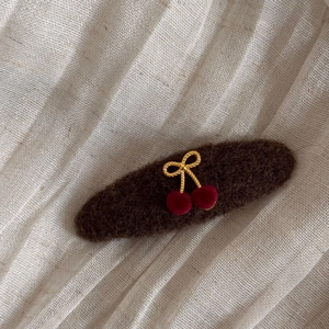 Detail of felt cherry bow hair clip with golden metallic accents and red flocking texture