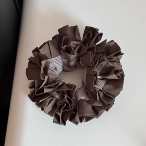 Macro detail of dark brown pleated hair scrunchie with satin texture on beige leather