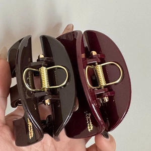 Detail of red and brown hair claws featuring golden signature logo and glossy finish