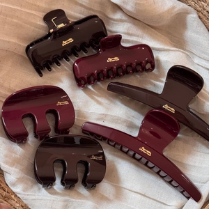 Detailed view of large burgundy hair claws with golden French lettering on linen