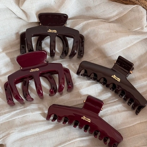 Detailed view of dark brown and wine red shark hair clips with golden brand logos