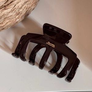 Close-up of a large brown hair claw clip with a polished finish and golden logo detail