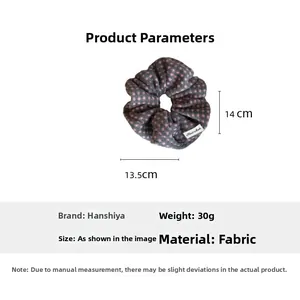 Detailed view of a grey polka dot scrunchie with 14cm dimensions and handmade label
