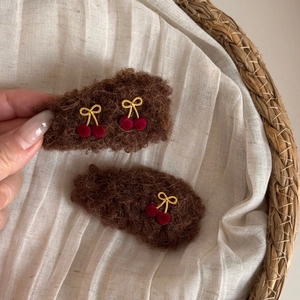 Detail of plush cherry BB hair clips with golden bows on white linen background