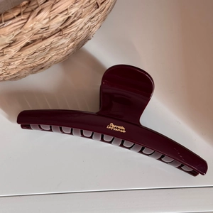 Detailed close-up of large burgundy hair claw clip with gold lettering on woven basket