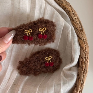 Detail of plush cherry hair clips featuring brown teddy fleece and red velvet pom-poms