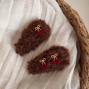Detailed view of plush brown cherry hair clips with golden bows on white fabric