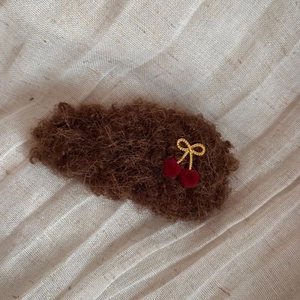 Detail of plush brown faux shearling hair clip with gold bow and red velvet cherries
