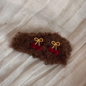 Detail of plush cherry earrings with golden woven metal bow and red velvet berries