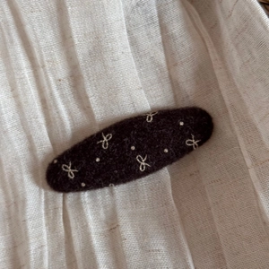 Detail of wool felt oval hair clip with creamy white bow embroidery and polka dots