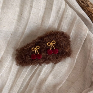 Close-up of elegant golden wire bow hair clips with dark red flocked cherry pendants