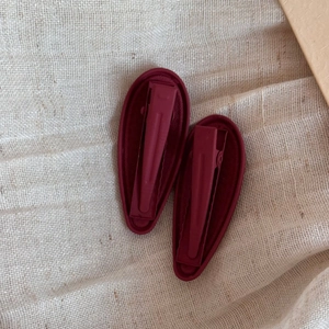 Macro detail of wine red teardrop hair clips featuring elegant wavy texture and matte finish