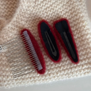 Close-up of red mohair hairpins and comb with silver metal teeth on a knit background