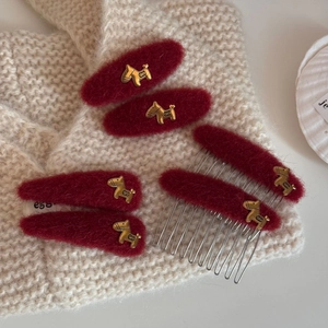 Detailed view of dark red plush hair clips with gold metal dog charms on knit fabric