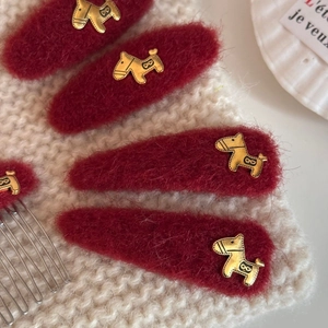Detailed view of burgundy plush hair clips with golden horse charms on a knitted background