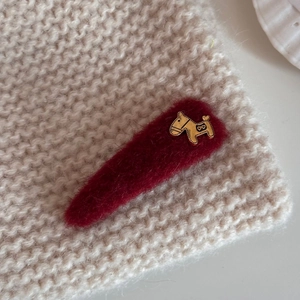 Detail of red plush hair clip with golden horse ornament on soft beige knit background