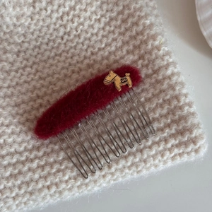 Close-up of red plush hair comb featuring a golden puppy charm on knit background