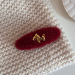 Detail of red plush hair clip with golden dog charm on cozy knit sweater background