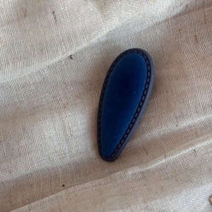 Detail of dark blue velvet teardrop hair clip with fine stitching on linen background