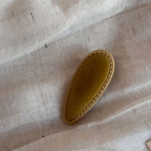 Detail view of vintage olive green velvet waterdrop hair clip on beige linen background